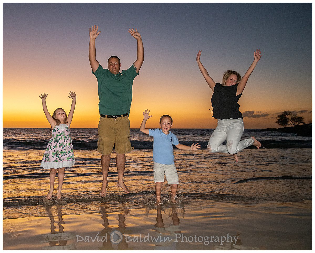 family takes a jump on the Mauna Kea beach at sunset